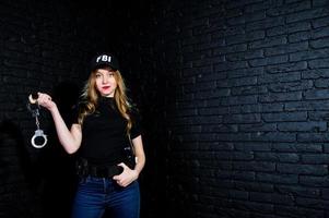 agente femminile dell'FBI in berretto e con la pistola in studio contro un muro di mattoni scuri. foto