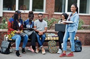 gruppo di cinque studenti universitari africani che trascorrono del tempo insieme nel campus nel cortile dell'università. amici afro neri che studiano al banco con articoli per la scuola, notebook portatili. foto