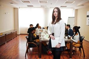 volto di bella donna d'affari europea, tenendo il laptop sullo sfondo della riunione del team multirazziale di uomini d'affari, seduto al tavolo dell'ufficio. foto