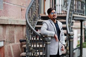 elegante uomo indiano con bindi sulla fronte e occhiali, indossa un abito posato all'aperto contro le scale di ferro. foto