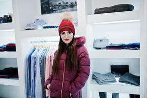 bruna splendida ragazza nella boutique del negozio di abbigliamento in giacca invernale rossa con cappello. foto