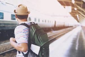 ritratto laterale di un giovane sorridente seduto con il telefono cellulare e la borsa in attesa del treno foto