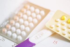 test di gravidanza positivo e pillole anticoncezionali alla data dello sfondo del calendario. concetto di controllo delle nascite di assistenza sanitaria e medicina. foto