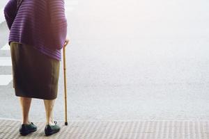 anziana donna anziana con bastone da passeggio in attesa sul marciapiede del marciapiede che attraversa la strada da sola. concetto senior dall'altra parte della strada alle strisce pedonali zebrate. foto