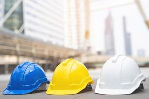 cappello per casco di sicurezza rigido bianco, giallo e blu per il progetto di sicurezza dell'operaio come ingegnere o lavoratore, su pavimento di cemento in città. foto