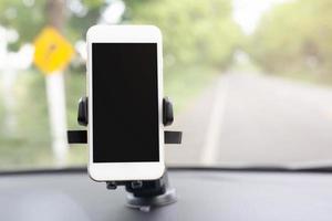 primo piano che tiene la mano utilizzando lo smartphone mobile con schermo nero nel supporto del parabrezza anteriore della console dell'auto. inserire la mappa di navigazione gps di viaggio sullo sfondo della plancia. copia spazio. foto