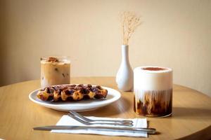 un pasto mattutino della domenica al bar, due tazze di caffè, latte macchiato al miele e eispanner americano serviti con waffle su piatto, decorato con vaso. foto