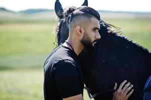 l'uomo arabo con barba alta indossa in nero con cavallo arabo. foto