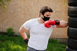 ritratto sport pugile arabo uomo in maschera medica nera boxe all'aperto durante la quarantena del coronavirus. foto