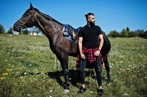 l'uomo arabo con barba alta indossa in nero con cavallo arabo. foto