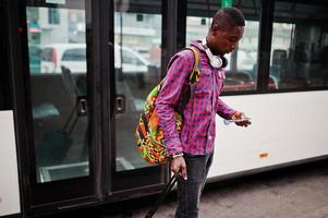 uomo afroamericano in camicia a scacchi, con valigia e zaino. viaggiatore nero contro autobus. foto