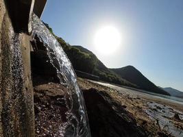 un piccolo corso d'acqua che cade nell'oceano con due montagne e un cielo blu sullo sfondo foto