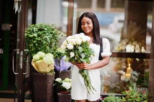 bella ragazza afroamericana con in mano un mazzo di fiori di rose bianche su appuntamenti in città. imprenditrice nera con un mazzo di fiori. foto