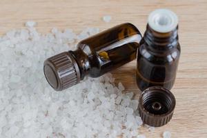 mucchio di sale marino e bottiglie con olio aromatico su tavola di legno. ingrediente naturale per spa ed esfoliazione. foto