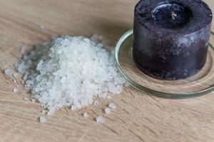mucchio di sale marino e candela nera sul tavolo di legno. ingrediente naturale per spa ed esfoliazione. foto
