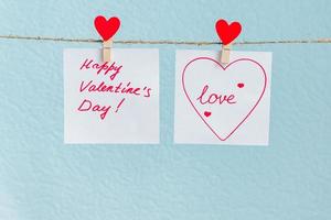 perno di cuori di amore di San Valentino rosso appeso al cavo naturale su sfondo blu. cuore disegnato su pezzo di carta. foto