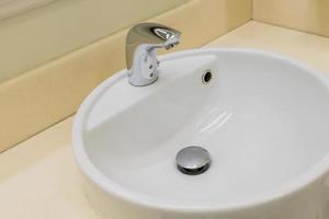 primo piano del lavello in ceramica bianca e del rubinetto in acciaio inossidabile nel bagno pubblico foto
