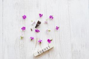 vista dall'alto del calendario in legno con segno di agosto, farfalla e fiori rosa. foto