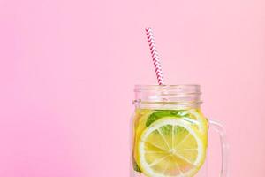 barattolo di vetro bicchiere di limonata fatta in casa con limoni, menta e paglia di carta rossa su sfondo rosa. bevanda rinfrescante estiva. foto