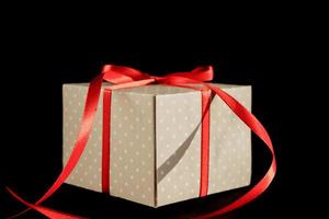 confezione regalo beige a pois con fiocco di nastro rosso su sfondo nero con spazio per la copia. foto