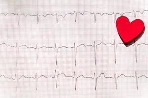 primo piano di un elettrocardiogramma in forma cartacea con cuore di legno rosso. sfondo di carta ecg o ekg. concetto medico e sanitario. foto