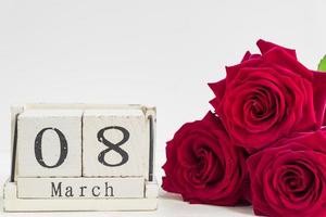 bellissimo bouquet di rose rosse e calendario cubo di legno su sfondo di legno. il concetto di congratulazioni per l'8 marzo o il giorno della donna. foto