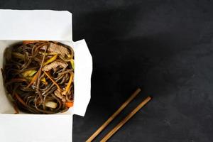 consegna di pranzi caldi in scatole. soba tagliatelle con carne di manzo e verdure su sfondo nero foto