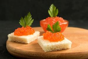 delizioso caviale rosso su pane di frumento servito con prezzemolo su scrivania in legno. foto