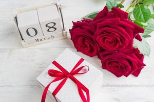 un regalo festivo, un bouquet di rose rosse e una confezione regalo su uno sfondo di legno. il concetto di congratulazioni per l'8 marzo o il giorno della donna. foto