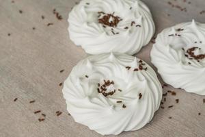 meringhe bianche fatte in casa e decorazioni di pasticceria al cioccolato su carta pergamena. foto