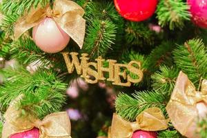 sfondo di natale e capodanno. primo piano di decorazioni per alberi di abete - palline rosse e rosa natalizie con fiocchi dorati e desideri giocattolo a forma di parola foto