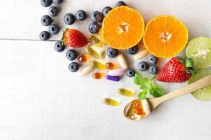 multivitaminici e integratori con frutta fresca e sana su fondo di legno bianco. foto