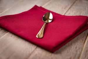 primo piano di un tovagliolo di stoffa di colore rosso e servito un cucchiaio da tè su un tavolo di legno. foto