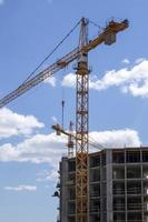 un' Lavorando costruzione Torre gru contro un' nuvoloso cielo su un' soleggiato giorno. il concetto di urbano sviluppo e costruzione. industriale sfondo. gru ingegneria, costruzione industria attrezzo. foto