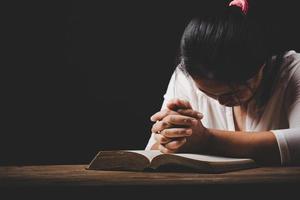 la mano della donna cristiana sulla Bibbia è pregare e adorare per ringraziare dio in chiesa con sfondo nero, concetto di fede, spiritualità e religione foto