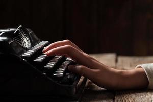 mani che scrivono sulla vecchia macchina da scrivere su sfondo di legno