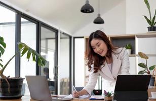 donna d'affari asiatica che utilizza un computer portatile e lavora in ufficio con il documento della calcolatrice sulla scrivania, facendo pianificazione analizzando il rapporto finanziario, investimento del business plan, concetto di analisi finanziaria. foto