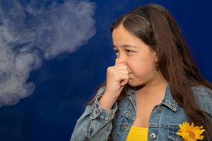 la ragazza adolescente si pizzica il naso perché i fumi tossici dell'auto, il cattivo odore, l'inquinamento atmosferico, le allergie alla polvere o l'infezione del seno, le adolescenti che si sfregano il naso soffrono di allergie in città, la vita delle persone urbane. foto