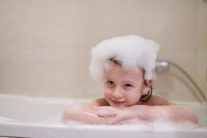 poco ragazza nel bagno giocando con sapone schiuma foto