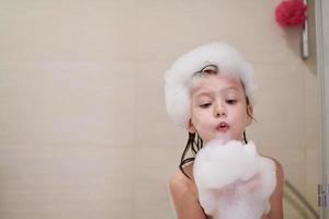 poco ragazza nel bagno giocando con sapone schiuma foto