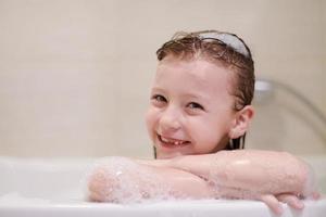 poco ragazza nel bagno giocando con sapone schiuma foto