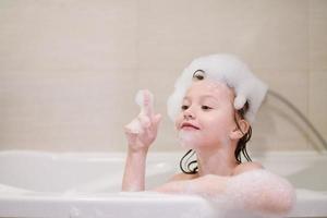 poco ragazza nel bagno giocando con sapone schiuma foto