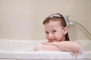 poco ragazza nel bagno giocando con sapone schiuma foto