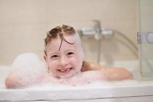 poco ragazza nel bagno giocando con sapone schiuma foto