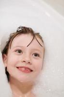 poco ragazza nel bagno giocando con sapone schiuma foto