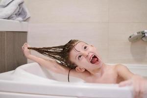 poco ragazza nel bagno giocando con sapone schiuma foto