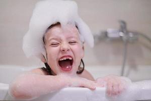 poco ragazza nel bagno giocando con sapone schiuma foto