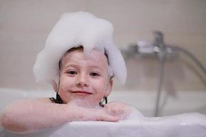 poco ragazza nel bagno giocando con sapone schiuma foto