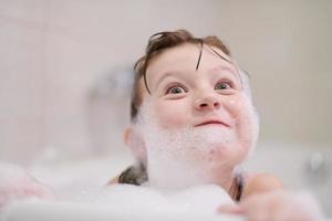 poco ragazza nel bagno giocando con sapone schiuma foto