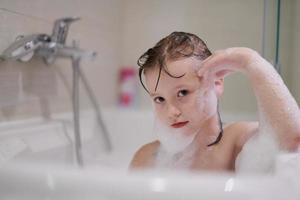 poco ragazza nel bagno giocando con sapone schiuma foto